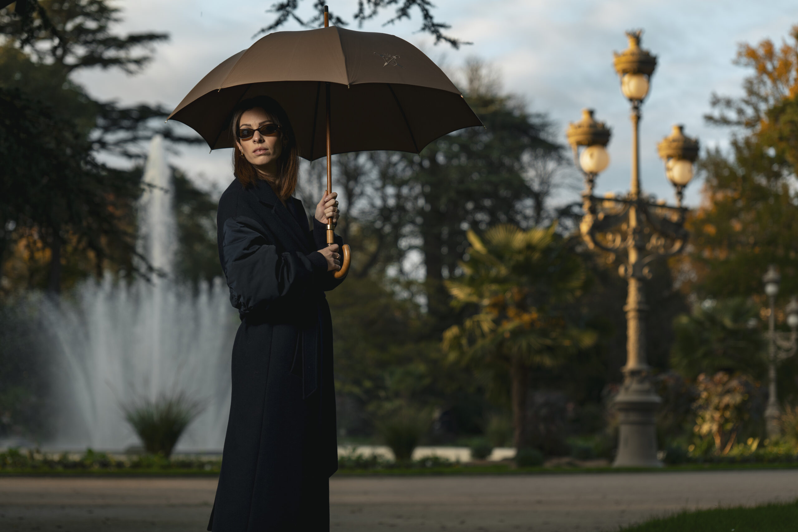 Portrait professionnel en extérieur d'une femme dans un parc à Toulouse posant de façon élégante avec un parapluie ouvert.