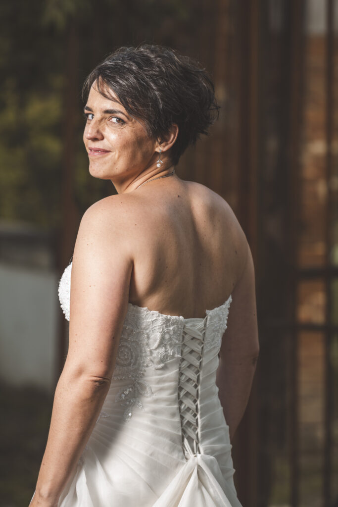 Portrait d’une mariée souriante en robe bustier blanche regardant par-dessus son épaule