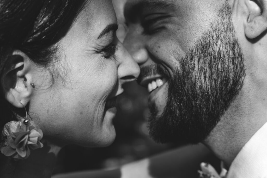 Un couple de mariés se sourit tendrement en gros plan. Leurs visages sont très proches, exprimant l’amour et la complicité. La photo en noir et blanc met en valeur l’émotion du moment.