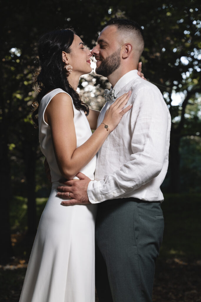 Jeunes mariés enlacés en pleine nature, échangeant un regard complice et tendre, éclairés par une lumière douce à travers les arbres lors d’une séance photo de mariage romantique en extérieur.
