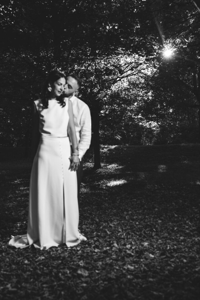 Couple de mariés dans une forêt baignée de lumière, photo en noir et blanc capturant un moment d’amour et de tendresse