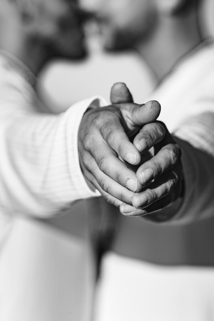 Gros plan en noir et blanc sur les mains entrelacées d’un couple d’hommes, symbolisant la force du lien et de l’amour partagé.