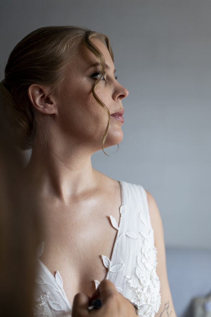 Photo de préparatifs de mariage : une mariée en robe blanche, mise en beauté avant la cérémonie, capturée sous une lumière douce et naturelle. Photographe de mariage à Toulouse.