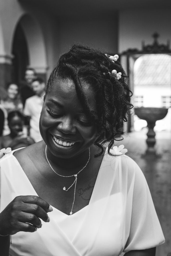 Photographie d'une mariée souriante dans une église en noir et blanc, rayonnante de bonheur lors de son mariage.