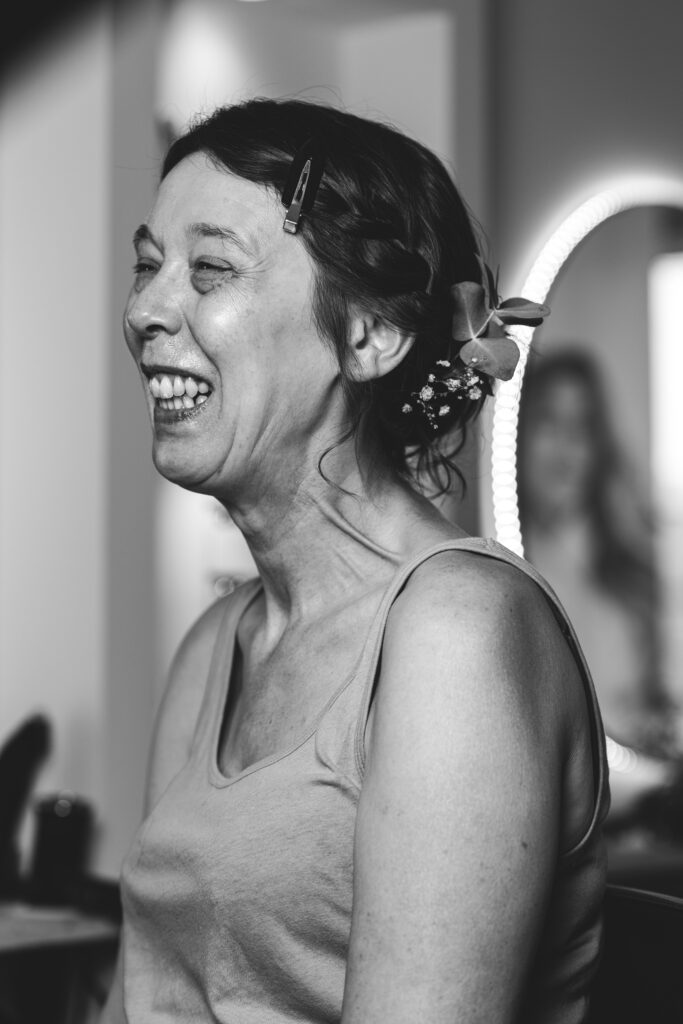 photographie d'une mariée en plein préparatif, éclatant de rire, capturée en noir et blanc.