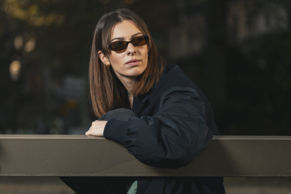 Portrait d'une femme en lunettes de soleil assise sur un banc, ambiance urbaine et moderne.