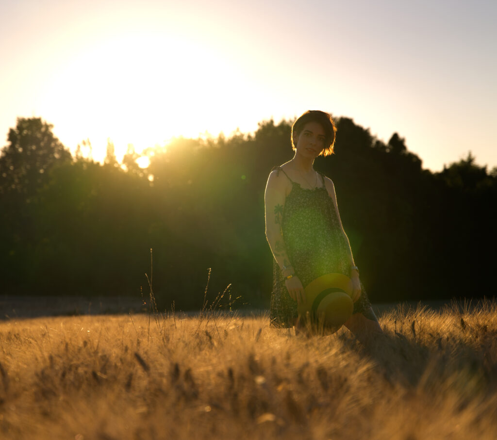 Portrait dans un champs de blé d'une femme chapeau à la main prise à contre-jour.
