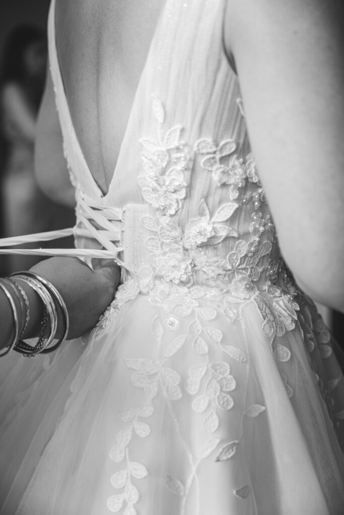 Photo des préparatifs de mariage, laçage du corset d’une robe élégante en dentelle. Instant intime capturé en noir et blanc à Toulouse.
